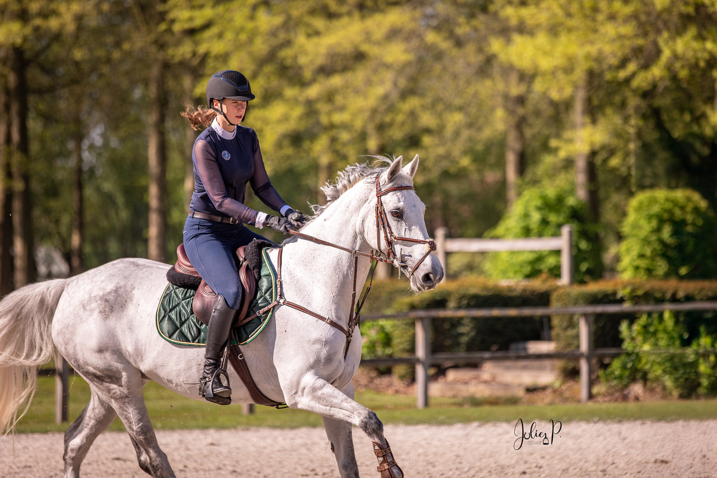 Vrouwelijke ruiter in FIR GREEN outfit rijdt op een grijze paard in een zonnige buitenomgeving