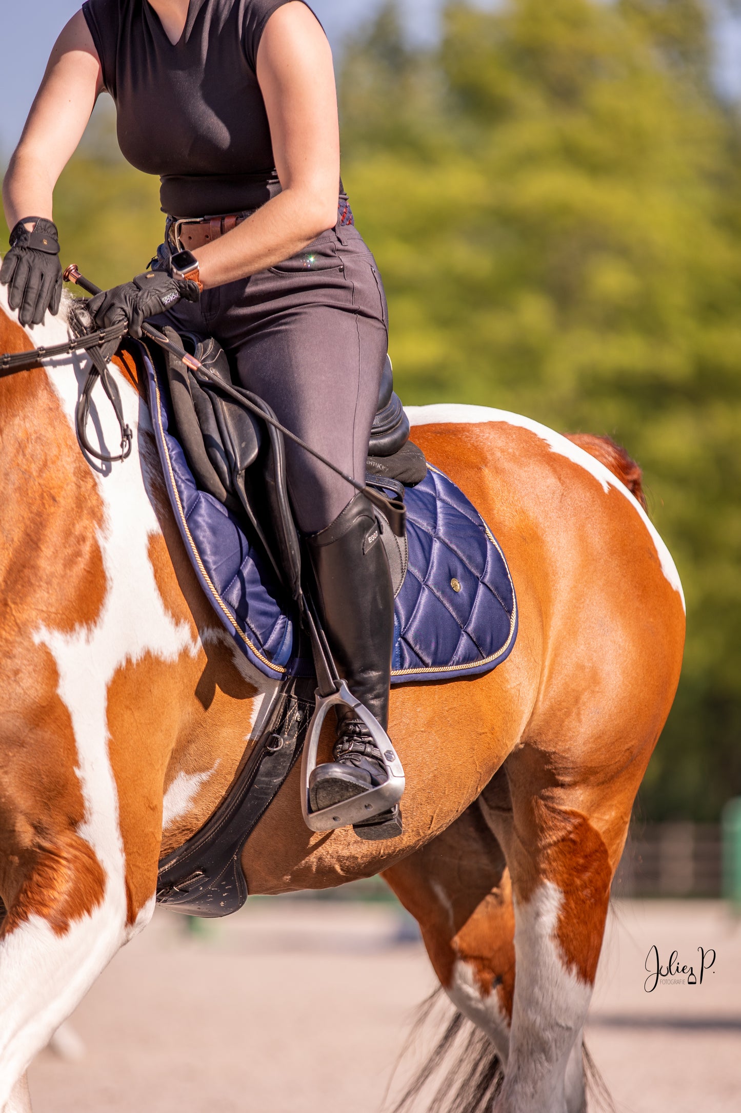 Paardrijdster in zwarte outfit met SPACE BLUE zadeldek op een schilderachtig paard