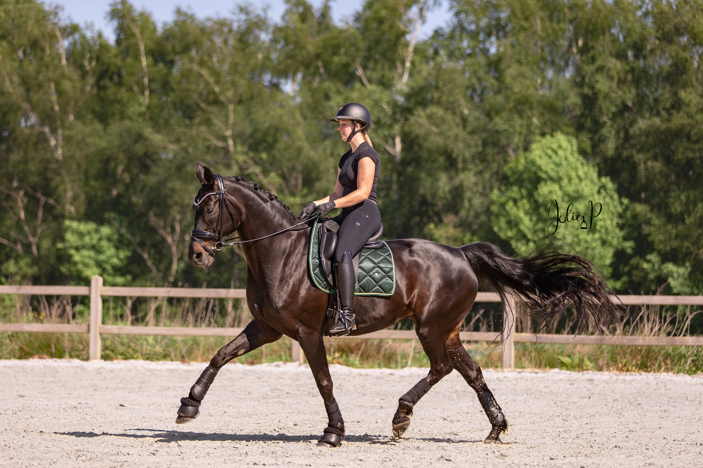 Ruiter in zwarte outfit op een paard met een FIR GREEN zadelpad in een rijbaan